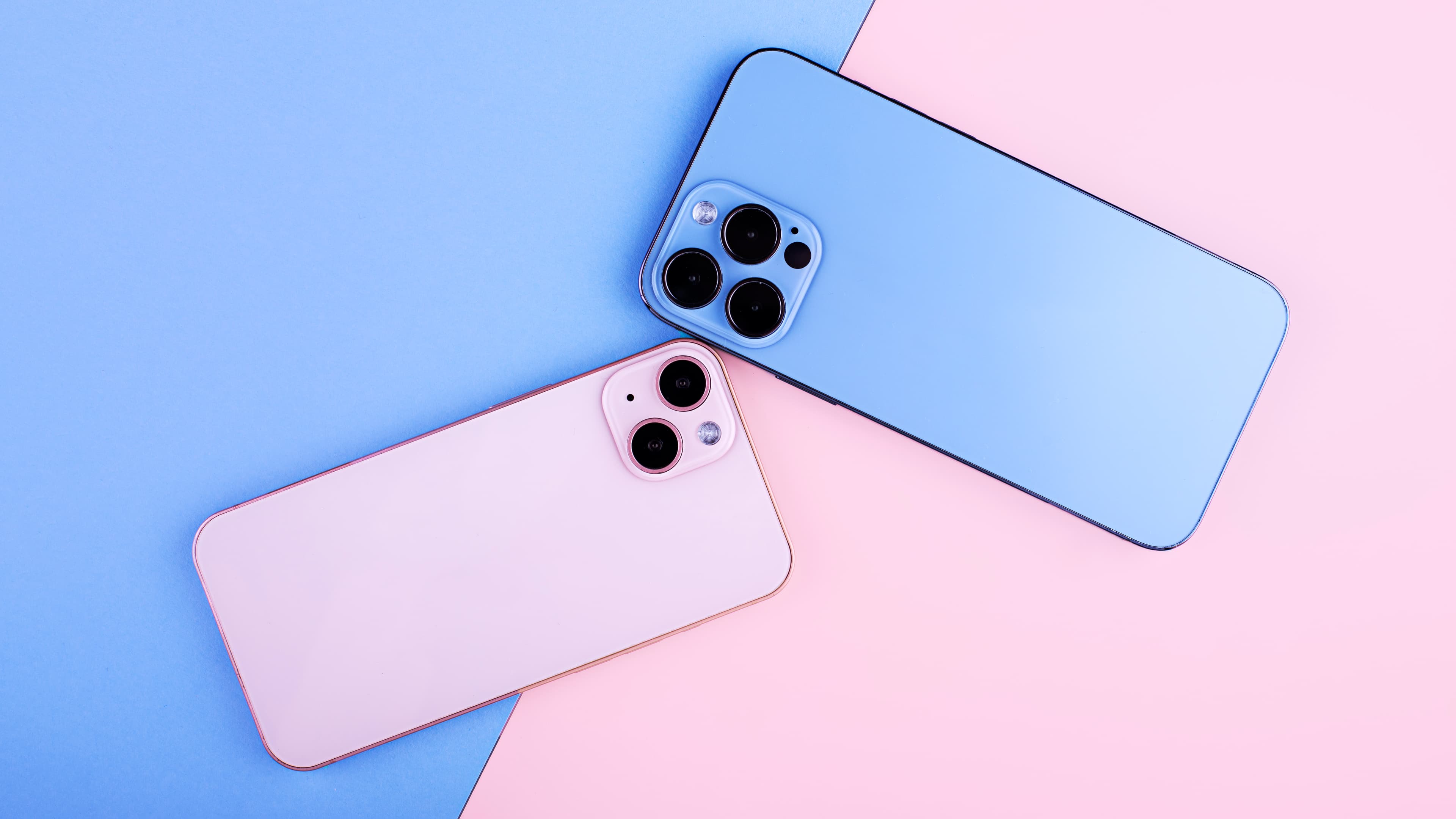 a pink and a blue smartphones laying face down on a pink and blue background